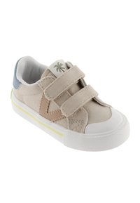 Zapatillas de lona beige con dos correas de Velcro, suela de goma blanca, acentos en verde y amarillo, y un pequeño diseño de palmera en la lengüeta.