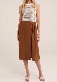 Brun midiklänning med texturerad tyg och ärmlös vit virkade överdel, med en sidodraperad detalj. Bärs med beige slidesandaler.