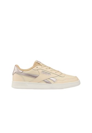 Zapatilla baja beige de Reebok con detalles metálicos plateados, diseño con cordones y suela de goma blanca sobre fondo blanco.
