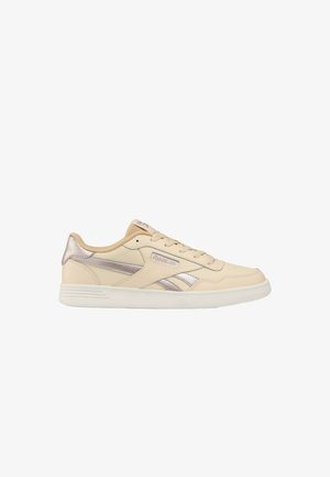 Beige lage Reebok sneaker met metallic zilveren accenten, vetersluiting en witte rubberen zool op een witte achtergrond.