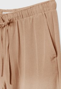 Close-up van beige linnen broek met elastische tailleband, trekkoord en zijzakken.
