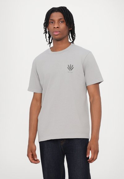 Gray cotton t-shirt with a round neck and short sleeves. Features a small black graphic on the left chest. Paired with dark blue jeans.