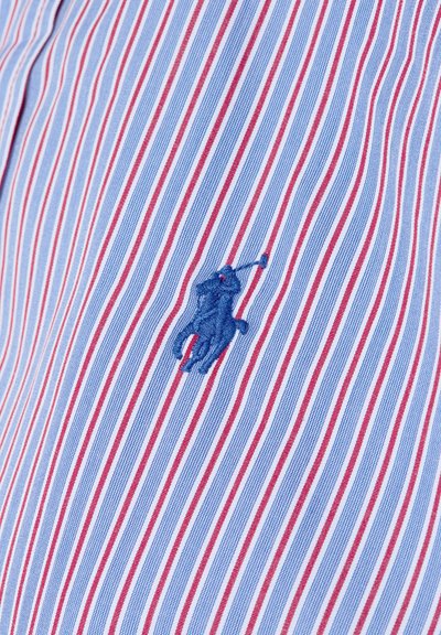Chemise rayée en bleu clair et rouge, avec des rayures verticales étroites. Logo brodé en bleu d'un cheval et d'un cavalier sur le côté gauche.