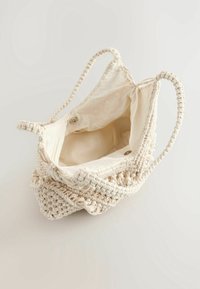 Macramé draagtas in off-white, met een geweven textuur en decoratieve kralenaccenten, stevige gevlochten handvatten en een stoffen voering met snap sluiting.