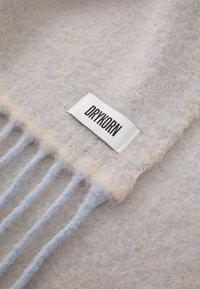 Sciarpa di lana leggera bluastro e beige con dettagli in frangia; etichetta cucita con "DRYKORN" in testo nero attaccata. Morbido al tatto.