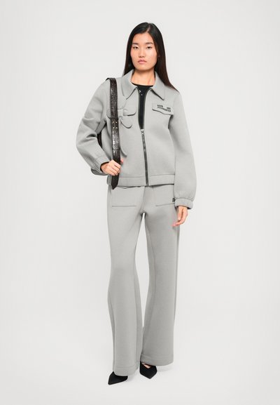 Gray zip-up jacket with a collared neckline and front pockets, paired with matching wide-leg pants. Model holding a textured black bag.