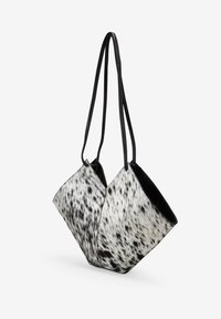 Bolso texturizado en piel de vaca en blanco y negro con un diseño angular único y dos largas correas negras para llevar.