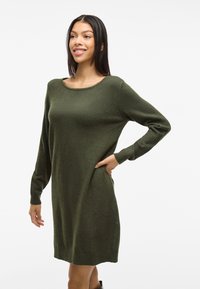 Abito in maglia verde con maniche lunghe, scollatura rotonda e polsini e orlo a coste. Il tessuto appare morbido e testurizzato. Nessun motivo visibile.