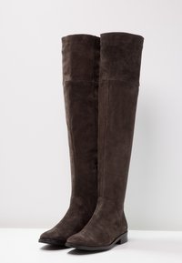 Knielange Stiefel aus dunkelbraunem Wildleder. Mit einem eleganten, taillierten Design, einer runden Zehenform und flacher Sohle, die eine glatte Textur zeigt.