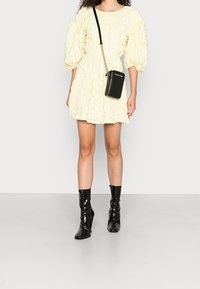 Kurzkleid aus leicht gelbem Textil mit Puffärmel, kombiniert mit schwarzen Lack-Ankle-Boots und einer kleinen schwarzen Umhängetasche.
