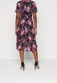 Svart klänning med rosa och vit abstrakt mönster, korta volangärmar, åtstramad midja och svängd nederdel. Matchad med svarta högklackade skor.