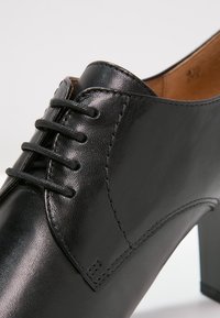 Chaussure en cuir noir avec une finition lisse, un design à lacets, une forme angulaire et un talon bloc modéré. Détails de couture accentués visibles.