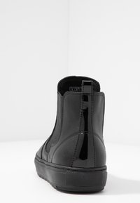 Stivaletto in pelle nera con pannelli laterali elastici, tab di estrazione verticale lucido sul retro e suola in gomma spessa, mostrato da un angolo posteriore.
