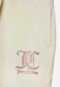 Um tecido de veludo creme com um logo bordado em rosa dourado. O design inclui um destacado "JC" e o nome da marca.