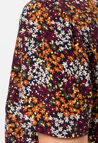 Tela con estampado floral en colores oscuros que presenta pequeñas flores naranjas, blancas y verdes sobre un fondo texturizado, con un detalle de mangas recogidas.