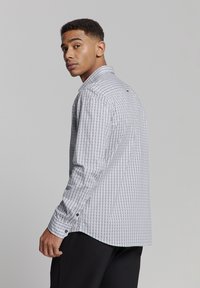 Witte langärmelige shirt met een geometrisch patroon in blauw en rood. Heeft een kraag en knoopmanchetten.