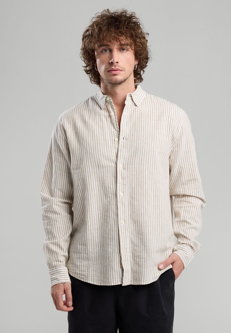 Camicia a righe crema e beige, design con bottoni, maniche lunghe, texture morbida, orlo curvo, piccolo dettaglio del logo vicino alla pattina dei bottoni.