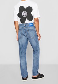 Camiseta blanca con un diseño de flor negra en la parte posterior, combinada con jeans de mezclilla azul claro que tienen una etiqueta azul y un corte relajado.