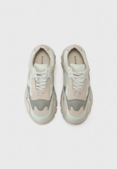 Sneakers featuring a mixed-material design in light green and beige, with a textured upper, padded collar, and logo detail on the tongue.