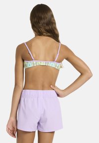 Shorts de bain lilas avec une ceinture élastique, associés à un haut bandeau multicolore présentant un motif logo. Texture de tissu lisse.