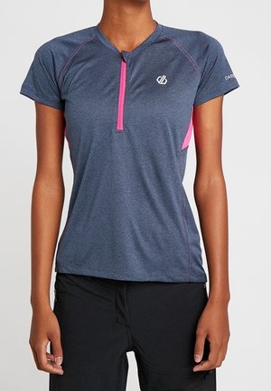 Vrouw draagt een donkergrijze atletische shirt met korte mouwen, een roze rits aan de voorkant en roze zijpanelen, gecombineerd met een zwarte broek.