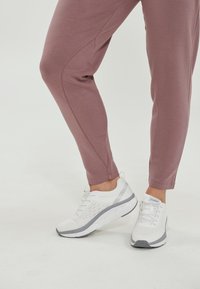 Ljusrosa träningsbyxor i kombination med vita sneakers med grå detaljer, nätöverdel, texturerad sula och snörningsdetalj.