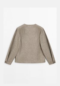 Béžové sako s dlouhým rukávem z texturované látky, s rovnými zády a knoflíkovými manžetami, položeno na rovné ploše na bílém pozadí.