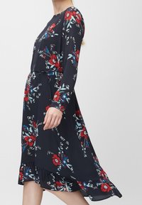 Långärmad marinblå klänning med ett blommönster i rött och blått. Har en volangkant och en avslappnad passform, tillverkad av ett mjukt tyg.