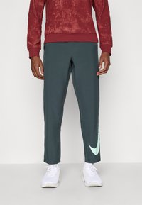 Nike sportbukser i mørkegrønn med en tapered design. Har en lys mint-logo på siden. Laget av glatt, pustende stoff.