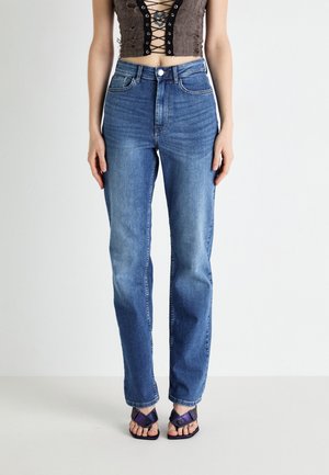 High-waisted blue denim jeans with a straight leg cut, light distressing, and subtle fading. Worn with black strappy sandals.