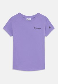 T-shirt lavande à manches courtes en tissu doux, avec un col rond et le logo "Champion" noir sur le devant et la manche.