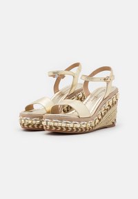 Sandali wedge in ecopelle dorata con piattaforma in juta intrecciata e cinturino. Presentano una fibbia e un design con punta aperta.