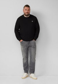 Felpa nera con un piccolo logo, jeans grigi e sneakers bianche. Vestibilità casual, materiale in cotone, con scollo rotondo e maniche lunghe.