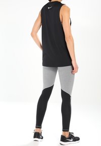 Sort ærmeløs atletisk tanktop med hvidt logo, parret med grå og sorte leggings med ribbet detaljer. Fodtøj: sorte sneakers.