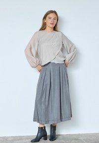Lysebeige, tekstureret bluse med lange, puffede ærmer og et draperet design, kombineret med et gråt plisseret nederdel og sorte ankelstøvler.