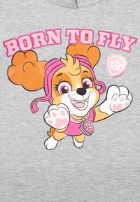 Camicia di tessuto grigia con un cane cartoon dalle orecchie arancioni, vestito rosa e un distintivo. Il testo recita "NATO PER VOLARE" in lettere rosa.