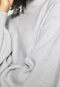 Pull gris à la texture douce, présentant un col montant et des manches volumineuses, mettant en avant une coupe décontractée et confortable.