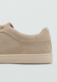 Beiger Wildledersneaker mit glatter Textur, abgerundeter Spitze und minimalistischem Design. Verfügt über eine Gummisohle mit feinen Nähten und Ösenakzenten.