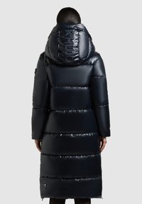 Geacă puffer de marină cu guler înalt și textură lucioasă. Prezintă cusături orizontale proeminente și detalii cu logo pe glugă.