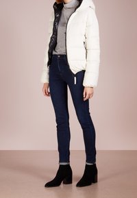 Doudoune blanche et noire avec capuche, associée à un jean skinny noir et des bottines à talons noires. Texture lisse et design matelassé.
