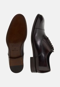 Scarpe eleganti in pelle nera con finitura lucida, punta rotonda, design con lacci e suola elegante con un accento marrone a contrasto.