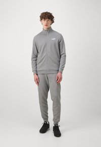 Survêtement de sport gris clair en tissu doux, comprenant une veste zippée à col montant et un pantalon fuselé assorti. Baskets noires incluses.