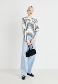 Stripet langermet skjorte i off-white og marineblå, parret med lyseblå vide jeans. Holder en liten svart håndveske med kjede-stropp.