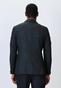 Maßgeschneiderte schwarze Sakko mit einer strukturierten, geometrischen Musterung. Verfügt über einen Schlitzausschnitt und gekerbte Revers. Schwarze Knöpfe vervollständigen das Design.