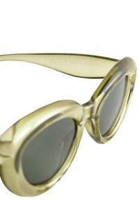 Gafas de sol transparentes en amarillo claro con lentes redondos de gran tamaño, que presentan un acabado brillante y sutiles detalles geométricos en la montura.