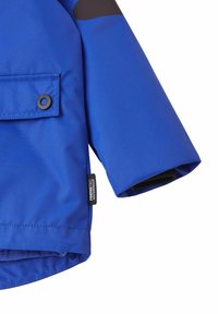 Ärmel und Tasche einer blauen wasserdichten Jacke mit schwarzem Druckknopf und einem Stoffetikett mit der Aufschrift „reimatec WATERPROOF“ auf weißem Hintergrund.