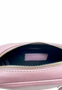 Interno di una borsa in pelle rosa con una cerniera dorata, caratterizzato da una texture liscia e un piccolo etichetta visibile nella fodera scura.