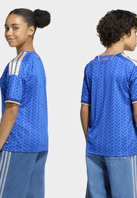 Blå tröja i andningsbart tyg, med ett texturerat lövmönster, gulddetaljer på axlarna och kontrasterande ärmslut.