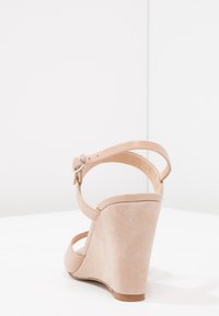 Beige klínové sandály se semišovým povrchem, nastavitelným páskem kolem kotníku, kulatou špičkou a klínovým podpatkem o výšce 10 cm. Plochá podrážka s minimálním zdobením.