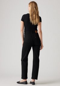 Jeans negros de tiro alto con un corte recto, parche de cuero en la parte trasera y un diseño minimalista. Combinados con una blusa negra ajustada y zapatos planos negros.